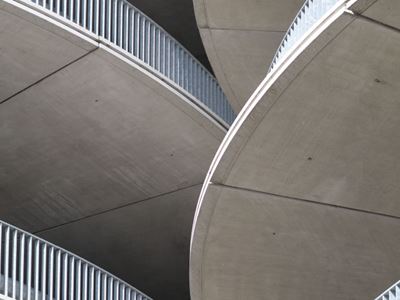 Abstract upward view of curved concrete ramps and metal railings in a multi-level parking structure.