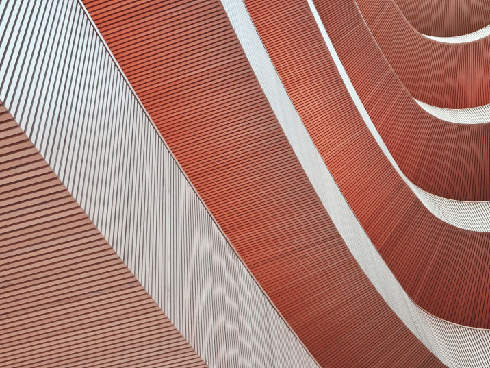 Abstract close-up of a modern building's curved facade with alternating red and white horizontal ridged panels.