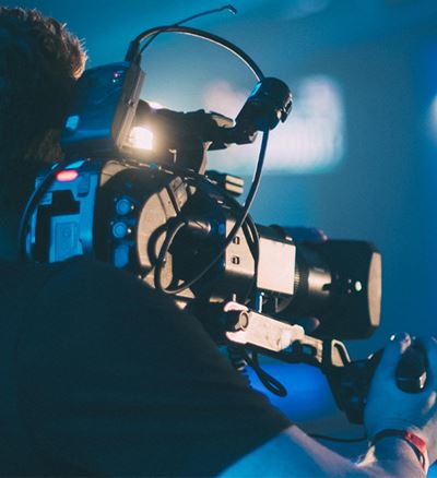Videographer filming a person in a blue-lit setting.