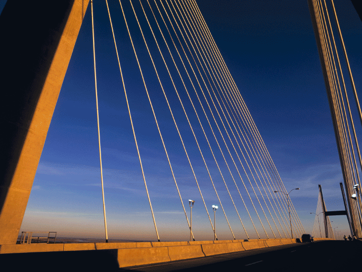 Close-up view of a cable-stayed suspension bridge at sunset, showing the towering support pylon and cables fanning out against a deep blue sky.