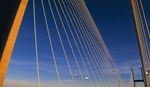 A suspension bridge with tall, illuminated cables against a deep blue twilight sky. The design conveys a sense of modernity and elegance.