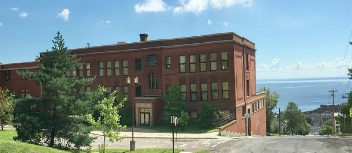 Red brick building with trees and a view of a water in the background