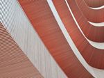 Primo piano astratto della facciata curva di un edificio moderno, caratterizzata dall'alternanza di pannelli orizzontali scanalati rossi e bianchi.