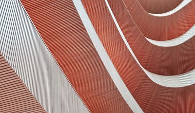 Dettaglio architettonico astratto che mostra superfici curve color terracotta con motivi geometrici lineari ed elementi strutturali bianchi.