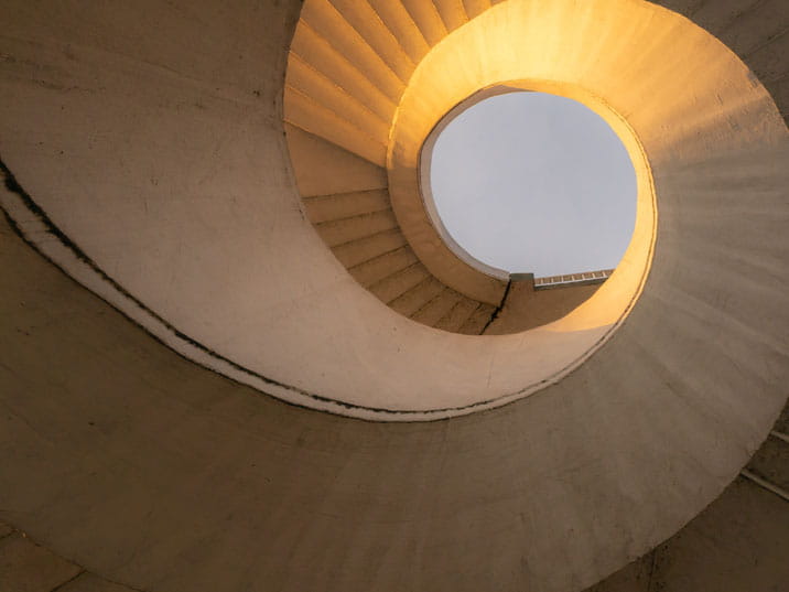 A spiral staircase illuminated by light streaming through, creating a warm and inviting atmosphere.