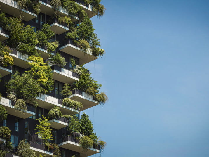 Moderno edificio a torre con alberi e piante rigogliose che crescono su diversi balconi.