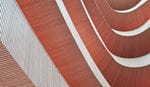 抽象的な建築細部。曲面状のテラコッタ色の表面に幾何学的な線模様が施され、白い構造要素が配されている。