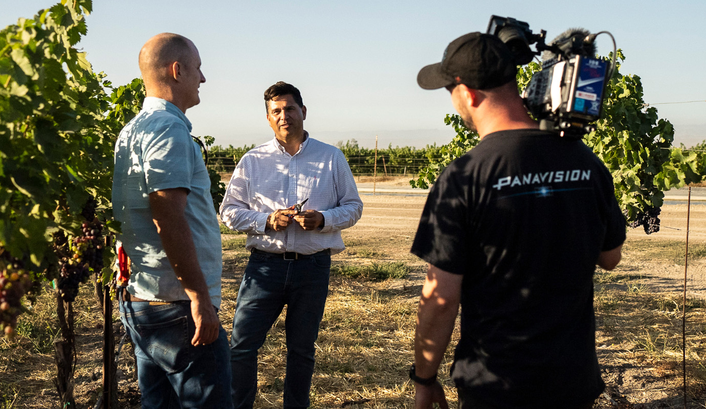 Man in a field talking to an interviewer with a camera